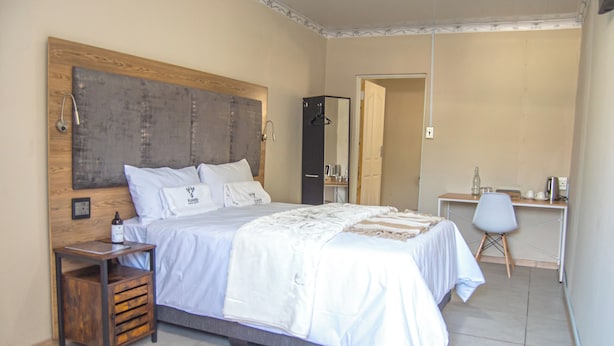 A bedroom with a bed, bedside table, wardrobe, and a desk with a chair. - Kololo at 399 Guesthouse & Conference (Welkom)