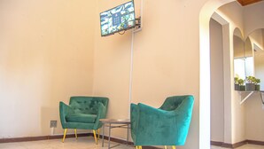 A lobby with two teal armchairs, a small round table, and a security camera mounted on the wall. - Kololo at 399 Guesthouse & Conference (Welkom)