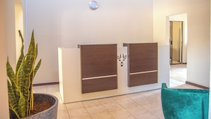 A reception area with a potted plant, a reception desk with a wooden finish, and a teal chair. - Kololo at 399 Guesthouse & Conference (Welkom)