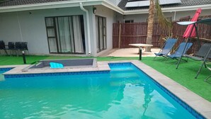 A rectangular swimming pool with a tiled edge, surrounded by a grassy area and a wooden fence. - Kololo at 399 Guesthouse & Conference (Welkom)