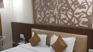 Una habitació d'hotel amb un llit gran, dos coixins, una tauleta de nit amb una làmpada i un panell decoratiu a la paret.