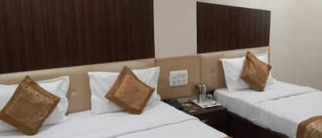 A hotel room with two beds, each with a wooden headboard, white bedding, and brown decorative pillows. There is a small table with a lamp, a telephone, and a remote control on the floor.