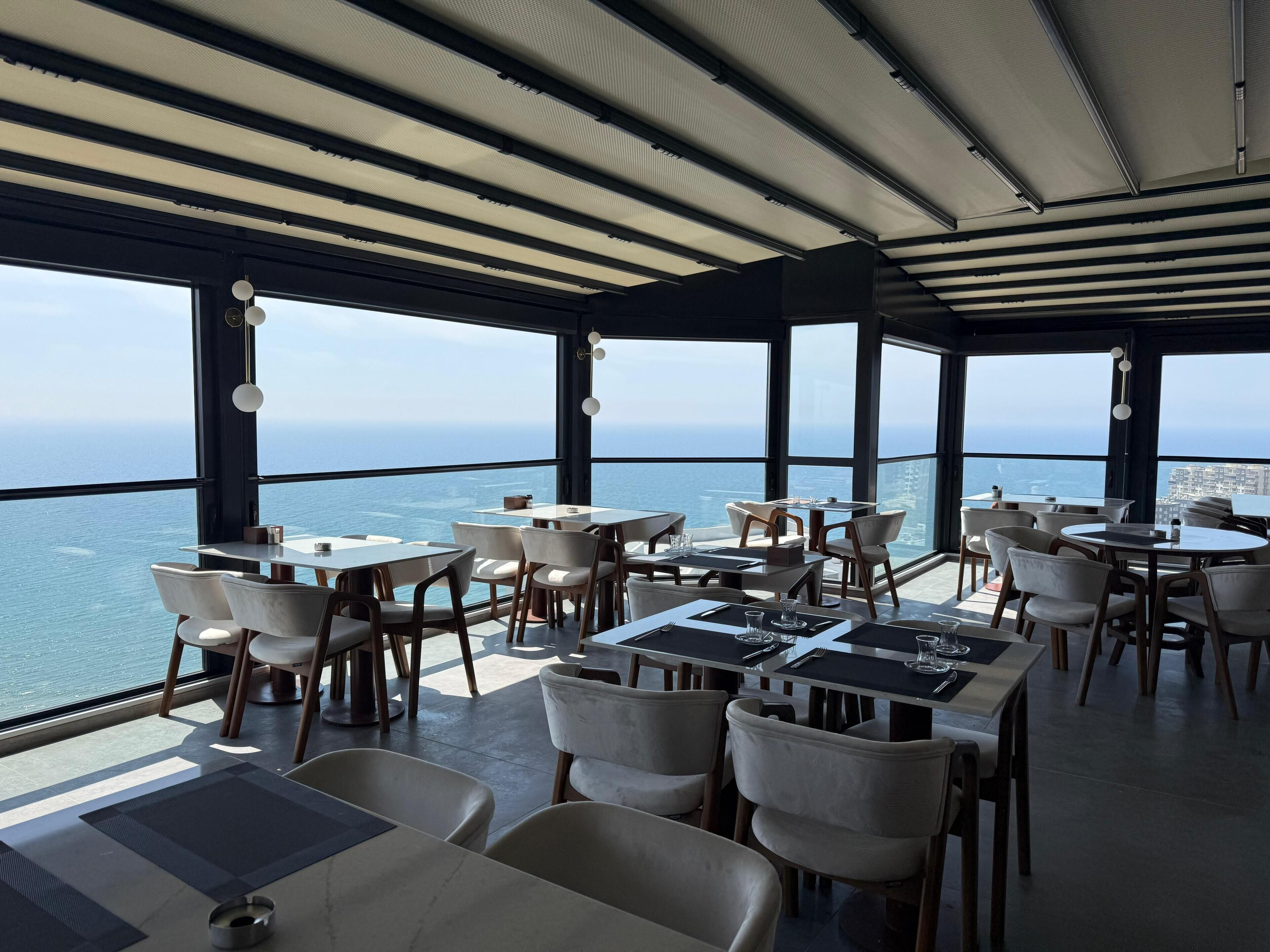 A restaurant with tables and chairs, large windows, and a view of the ocean.