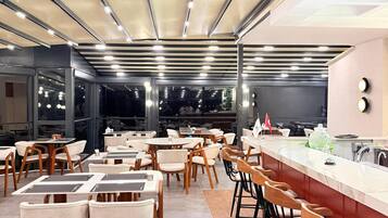 A modern restaurant with a long counter, multiple seating areas, and a high ceiling with strip lighting.