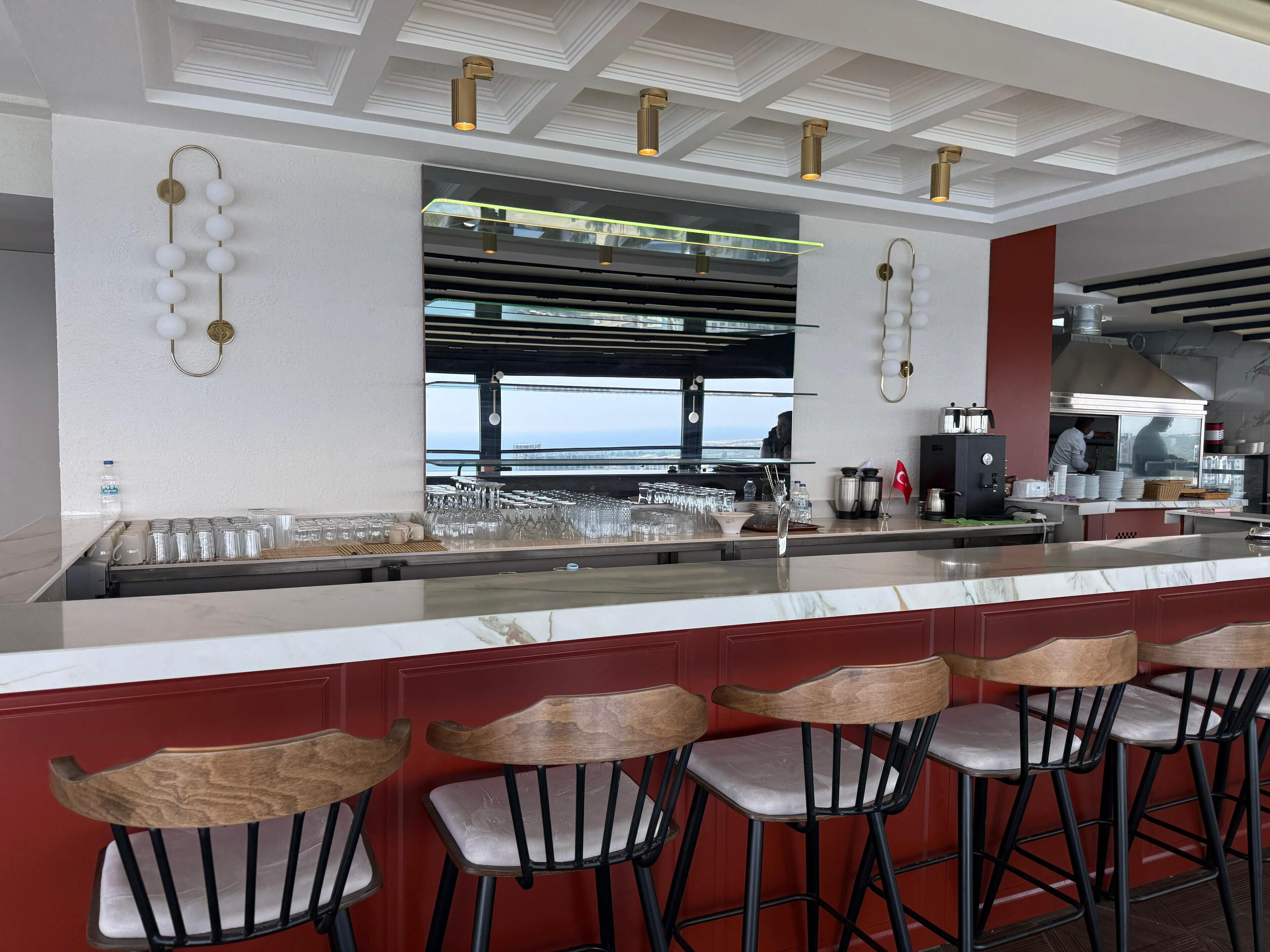 Uma área de bar moderna com bancada de mármore, banquetas e vista para o mar.