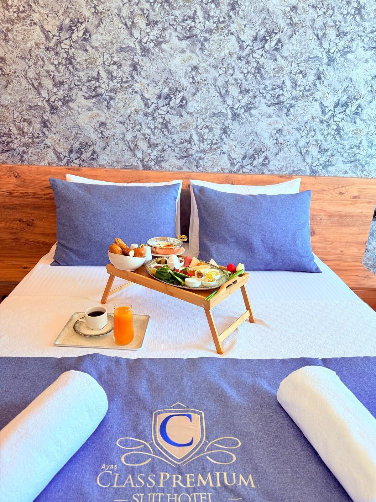 Een hotelkamer met een bed, twee kussens, een dienblad met ontbijt, een kop koffie en een glas sinaasappelsap.