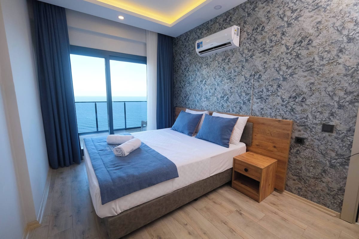 Une chambre moderne avec un grand lit, une table de chevet, un appareil de climatisation et une vue sur la mer grâce à une grande fenêtre.