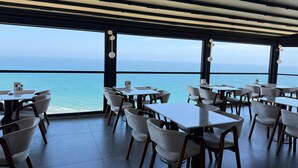 A restaurant with tables and chairs arranged for dining, large windows offering a view of the sea, and a ceiling with linear lighting fixtures. - Class Premium Hotel (Erdemli)