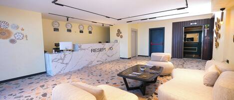 A hotel lobby with a reception desk, seating area, and a patterned floor.