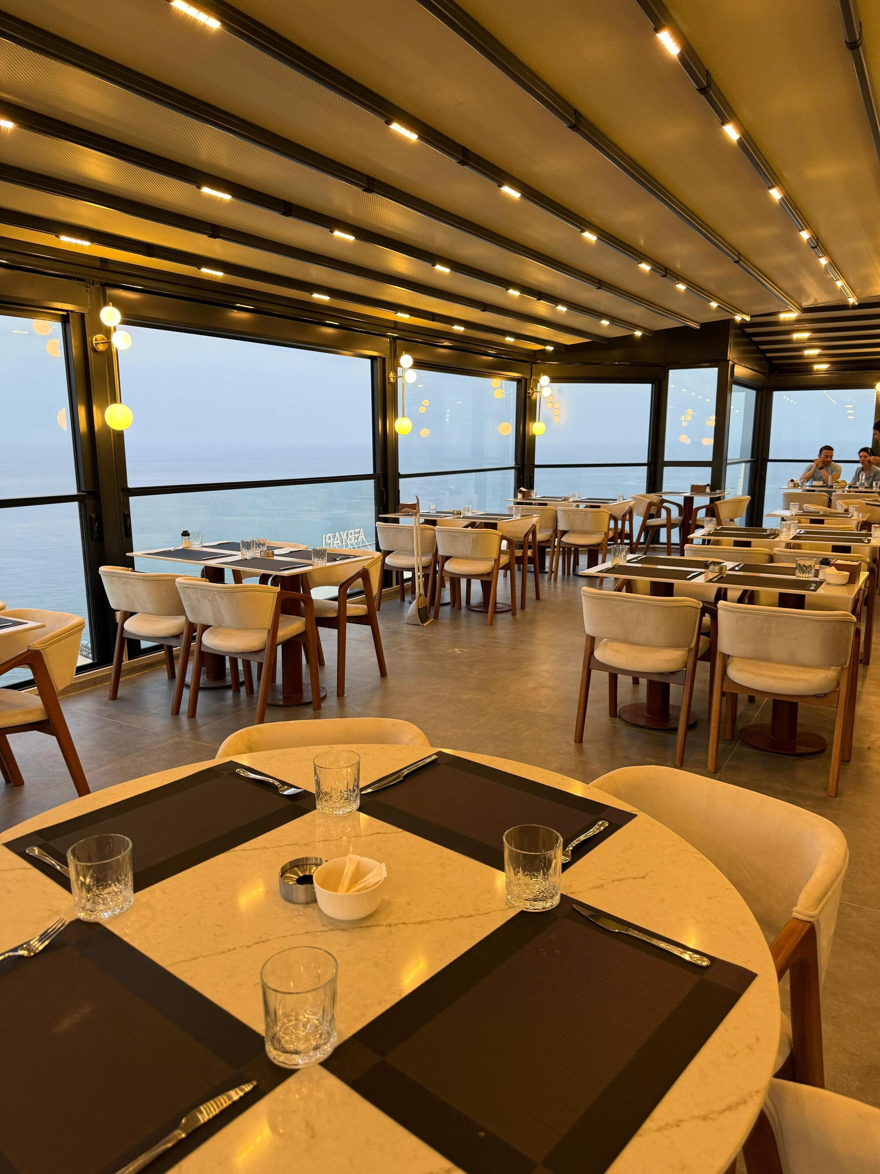 A restaurant with round tables, chairs, and a view of the sea.