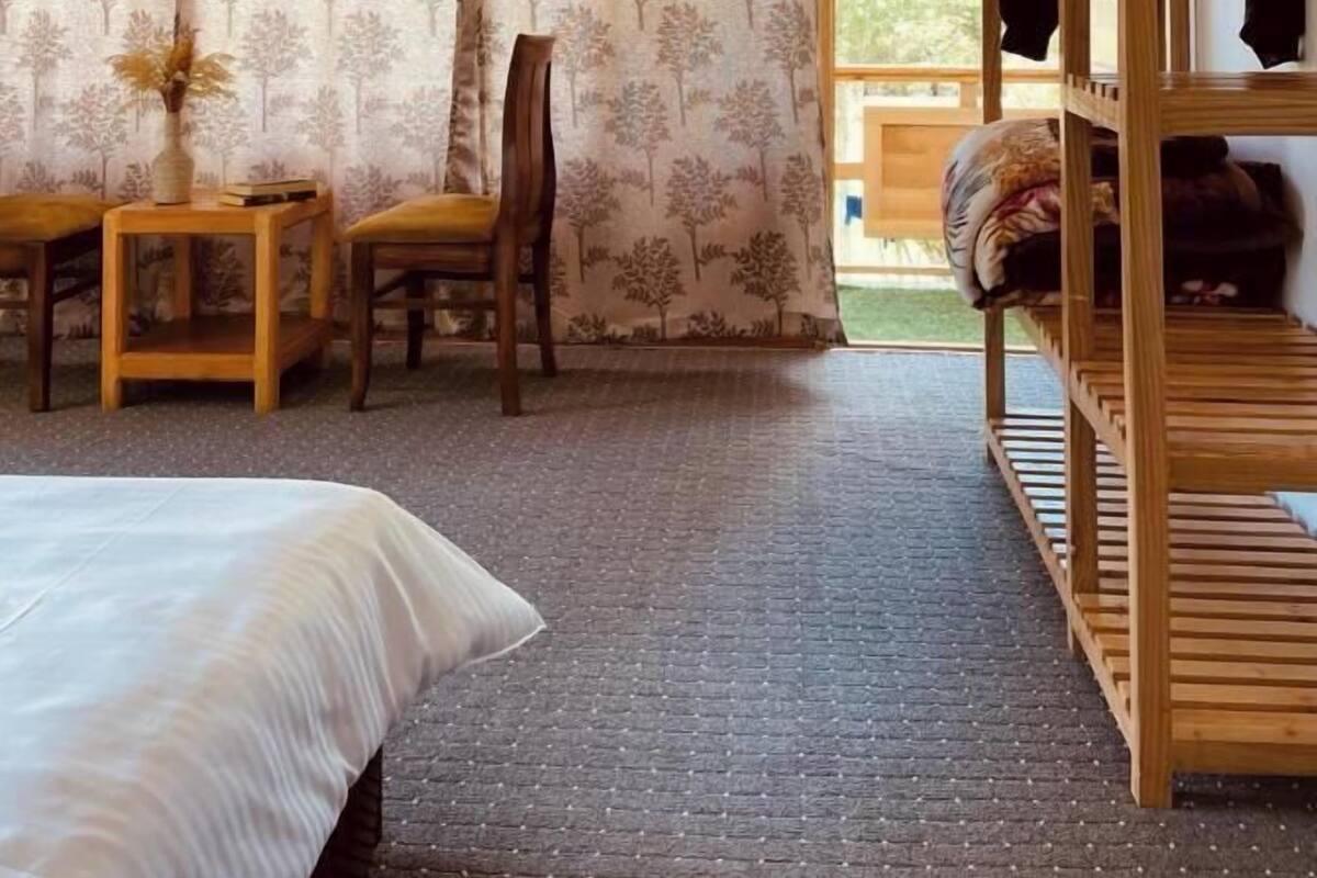 A bedroom with a bed, a wooden chair, a small table with a vase, and a wooden wardrobe.