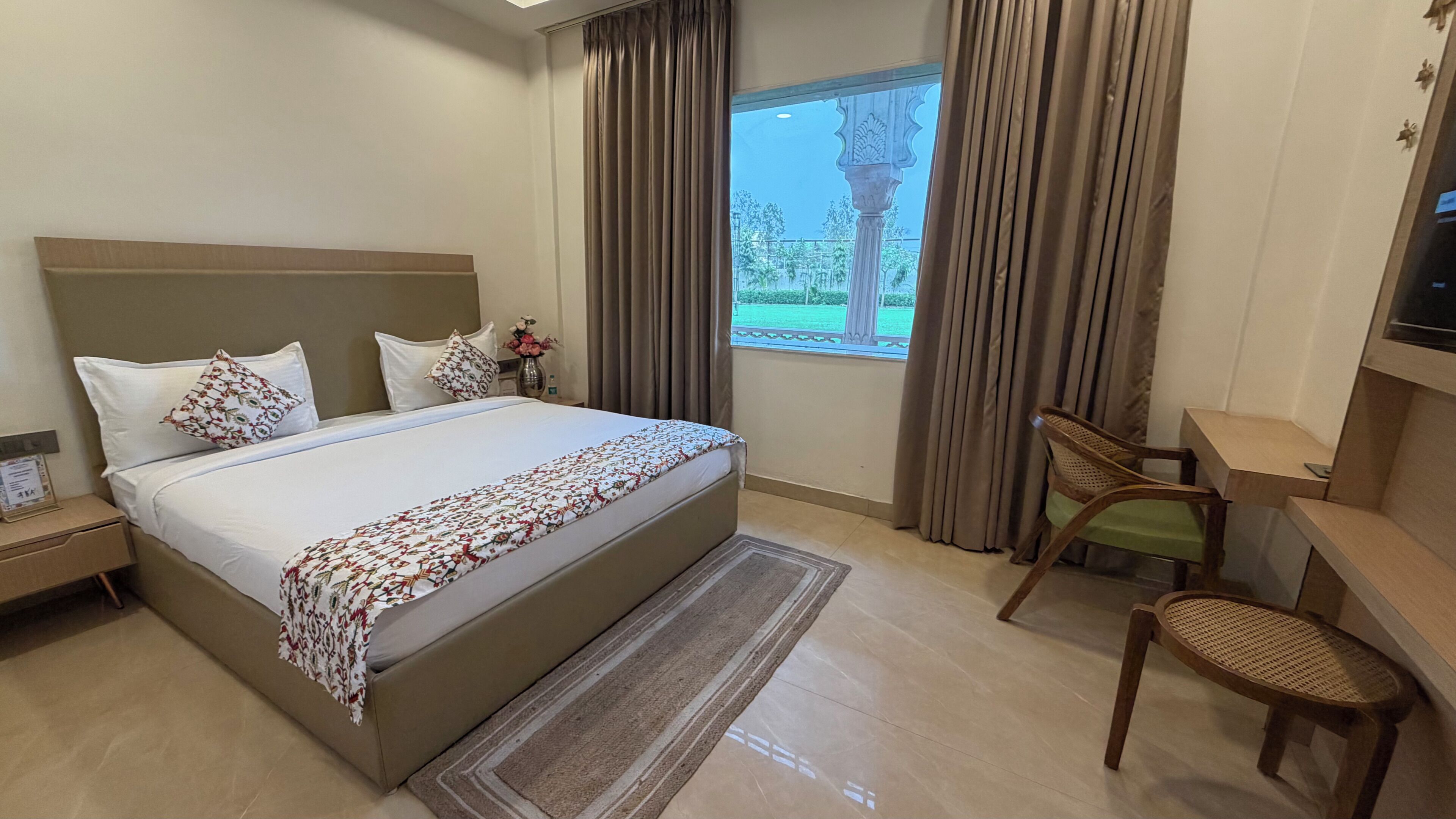 A hotel room with a bed, a desk, a chair, a nightstand, and a window with curtains.
