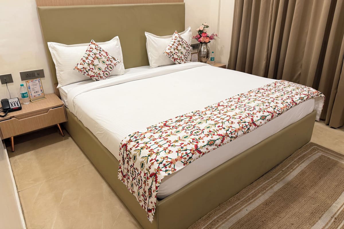 A hotel room with a bed, nightstand, and a vase with flowers.