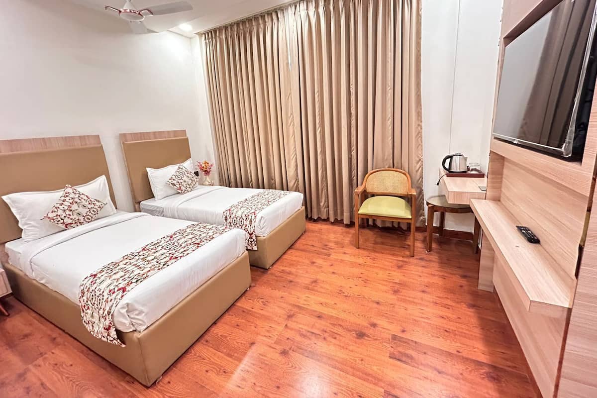 A hotel room with two beds, a desk, a chair, a TV, and a ceiling fan.