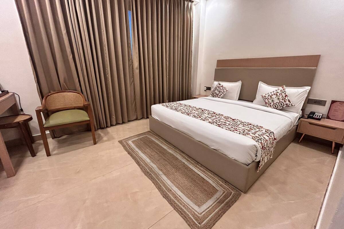 A hotel room with a bed, a chair, a desk, and a large window with curtains.