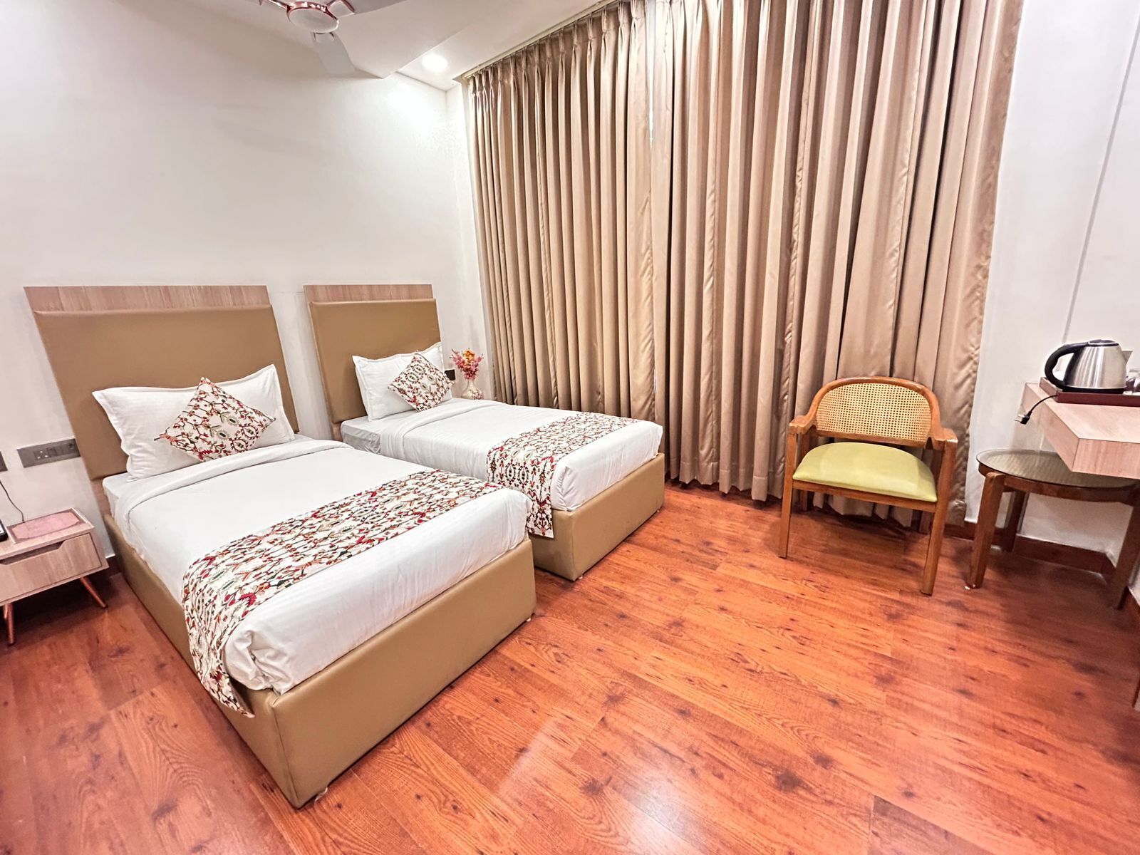 Habitación de hotel con dos camas, suelo de madera, una silla, un escritorio y una cortina.