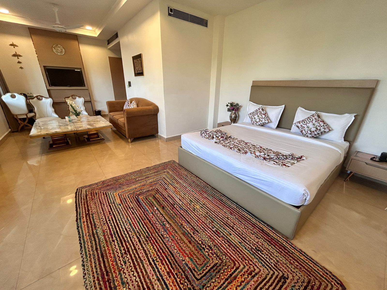 Ein Hotelzimmer mit einem Bett, einem Esstisch, Stühlen, einer Couch und einem Fernseher.