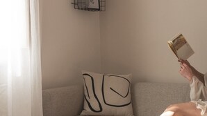 Une personne est assise sur un canapé gris, avec un coussin noir à motifs abstraits, et lit un livre.