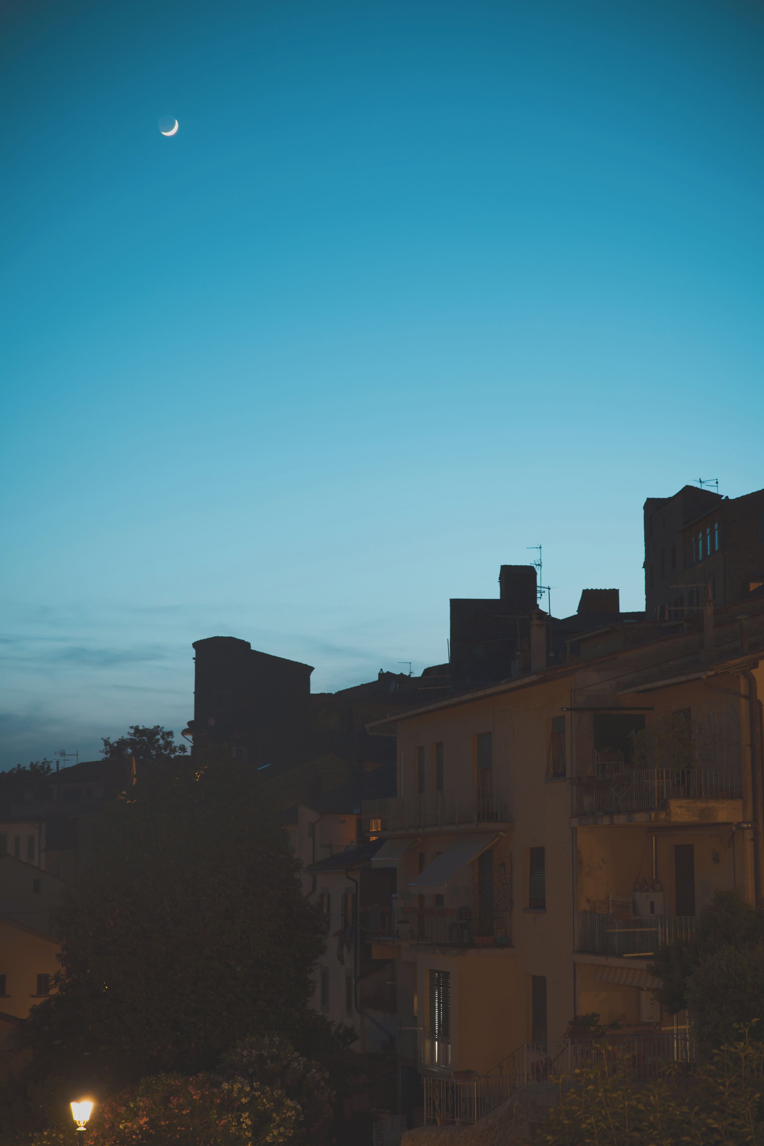 Una vista notturna di una zona residenziale con edifici e una luna crescente nel cielo.