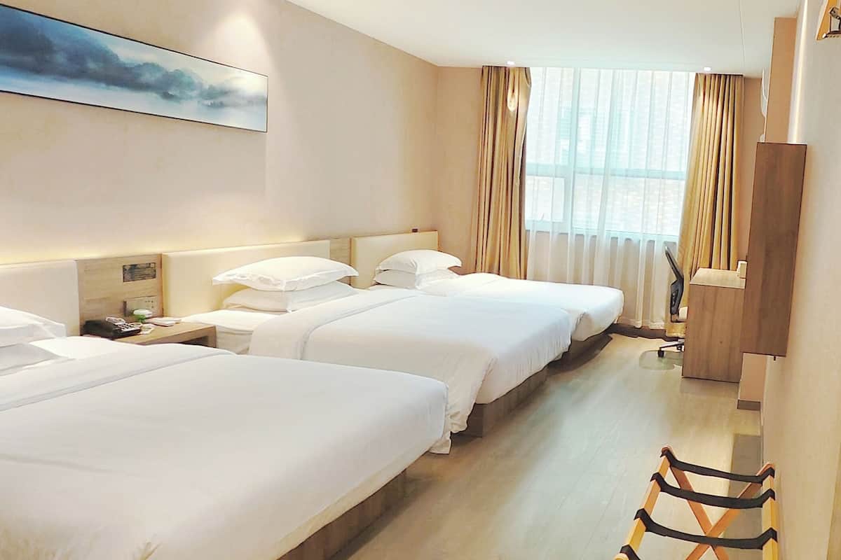 A hotel room with three beds, a wooden floor, a large window with curtains, and a painting on the wall.