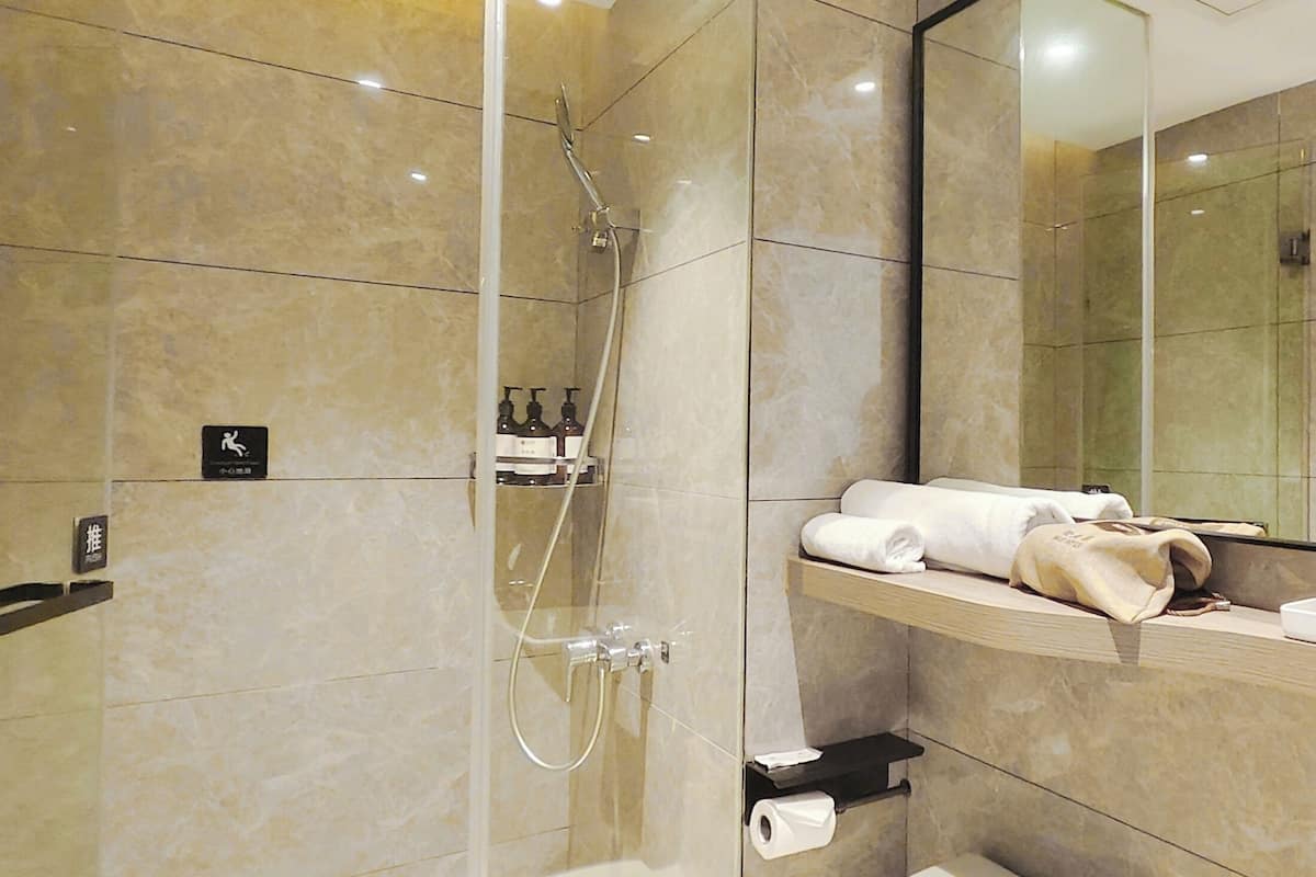 A modern bathroom with a glass-enclosed shower, a large mirror, and a vanity with toiletries.