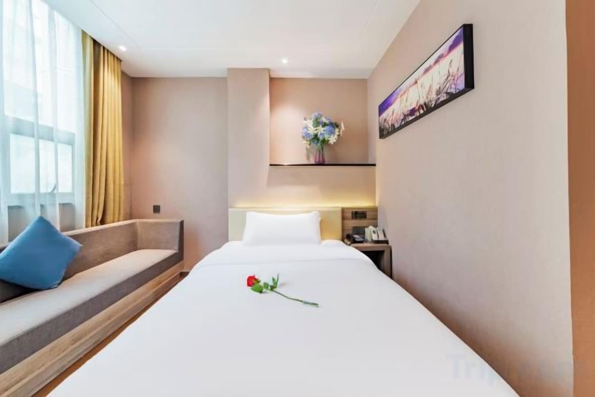 Une chambre d’hôtel avec un lit, un canapé, une table de chevet, une lampe et un tableau au mur.