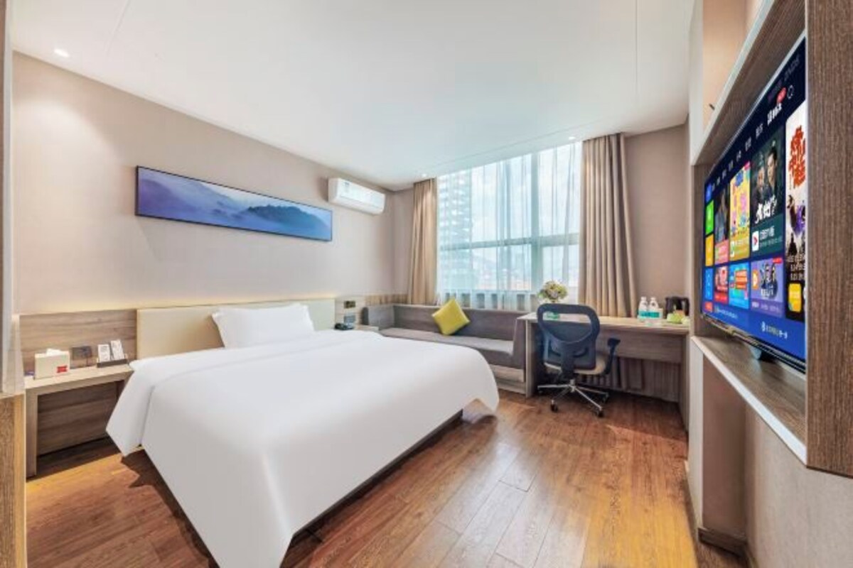 A hotel room with a bed, a desk, a chair, a TV, and a window with curtains.