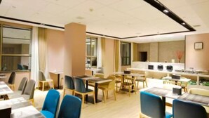 Un espace de restauration d’hôtel comprenant plusieurs tables et chaises, un coin cuisine et de grandes fenêtres.