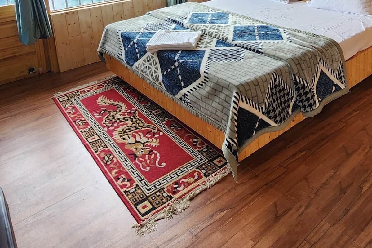 Un dormitorio con cabecera de madera, una cama grande con ropa de cama estampada, una alfombra roja y dorada, y vistas a montañas a través de una ventana con cortinas.