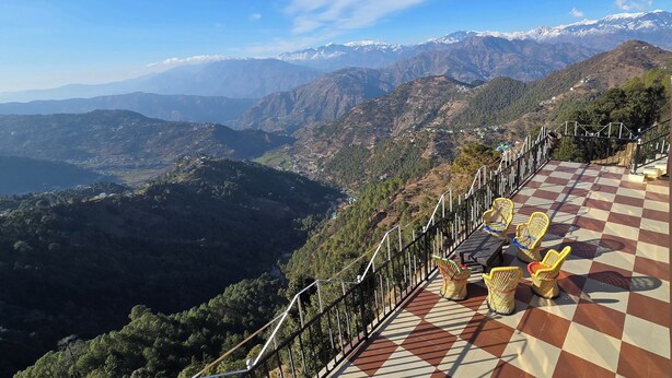 A scenic overlook with a checkered floor and wicker chairs, overlooking a mountainous landscape with snow-capped peaks. - Hotel HILL Mount View Dalhousie Chamba  (Dalhousie)