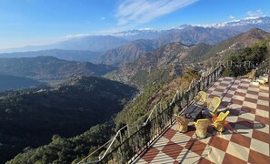 A scenic overlook with a checkered floor and wicker chairs, overlooking a mountainous landscape with snow-capped peaks. - Hotel HILL Mount View Dalhousie Chamba  (Dalhousie)