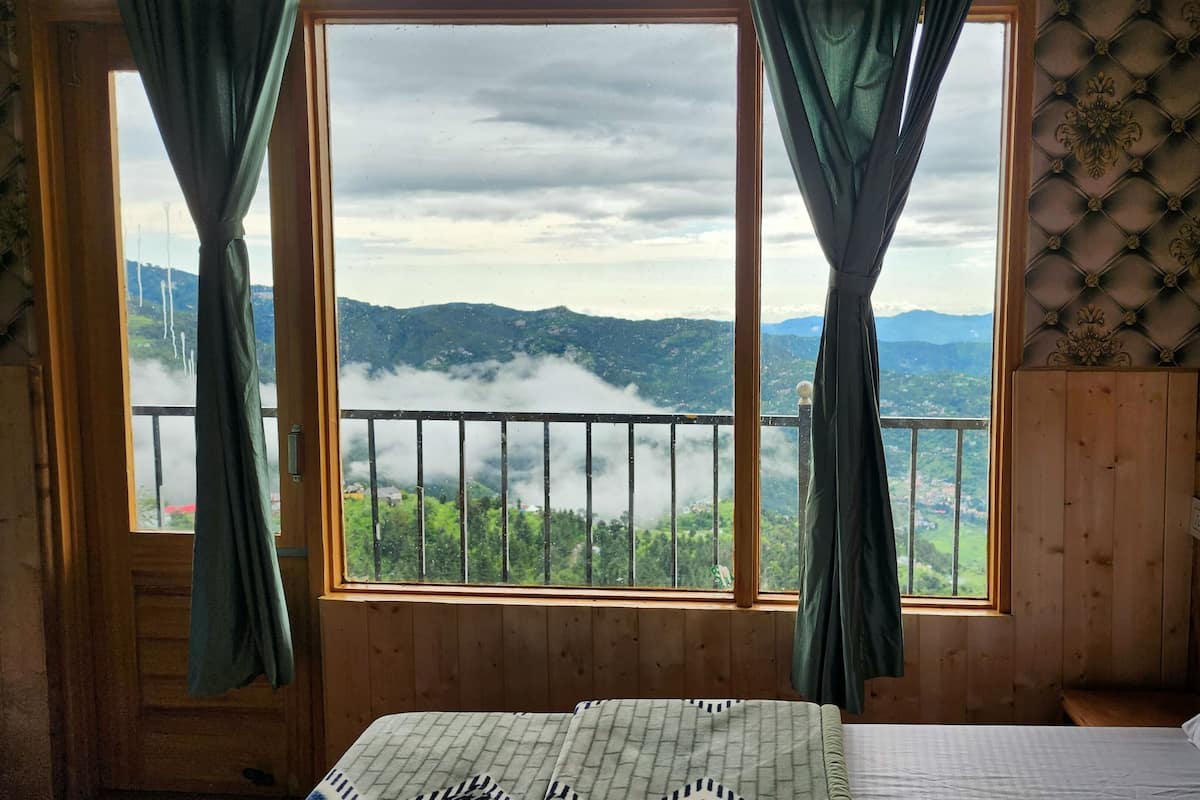 Habitación con cama, paredes de madera, vistas a montañas y un lago a través de un amplio ventanal con cortinas.