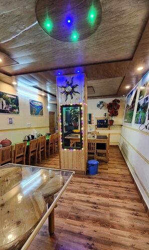 A cozy restaurant with wooden floors, a central dining table, and a decorative mirror with lights. - Hotel HILL Mount View Dalhousie Chamba  (Dalhousie)