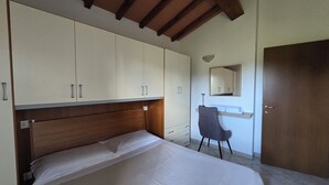 A bedroom with a wooden headboard, a bed, a desk with a chair, a wardrobe, and a door. - Val D'Orcia Window. Panoramic balcony. Pool. (Contignano)