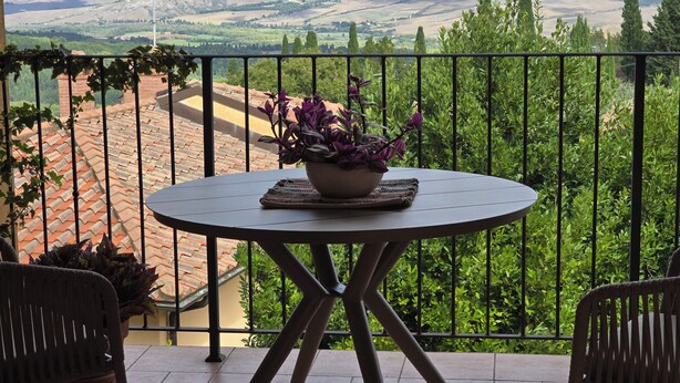 A balcony with a round table, chairs, and a potted plant. - Val D'Orcia Window. Panoramic balcony. Pool. (Contignano)