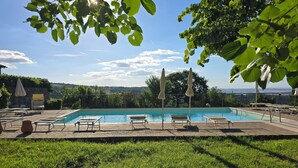 A pool area with lounge chairs and umbrellas, surrounded by greenery and a clear sky. - Val D'Orcia Window. Panoramic balcony. Pool. (Contignano)