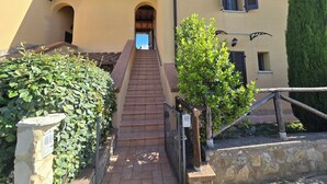 A building with a staircase leading to an entrance, surrounded by greenery and stone walls. - Val D'Orcia Window. Panoramic balcony. Pool. (Contignano)