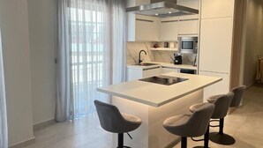 Ett modernt kök med en central köksö, barstolar, en mikrovågsugn och en fläktkåpa i rostfritt stål.