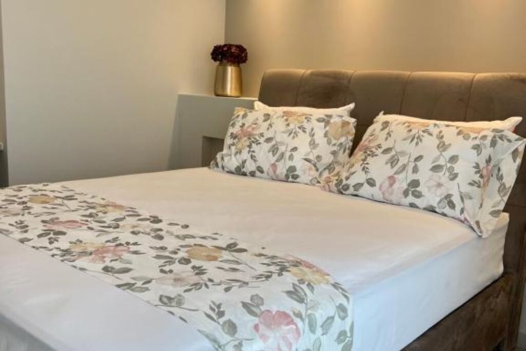 Una cama con ropa de cama floral, una mesita de noche con un florero y un cabecero marrón.