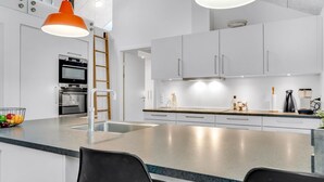 Ett modernt kök med vita skåp, rostfria vitvaror och en central köksö med sittplatser.