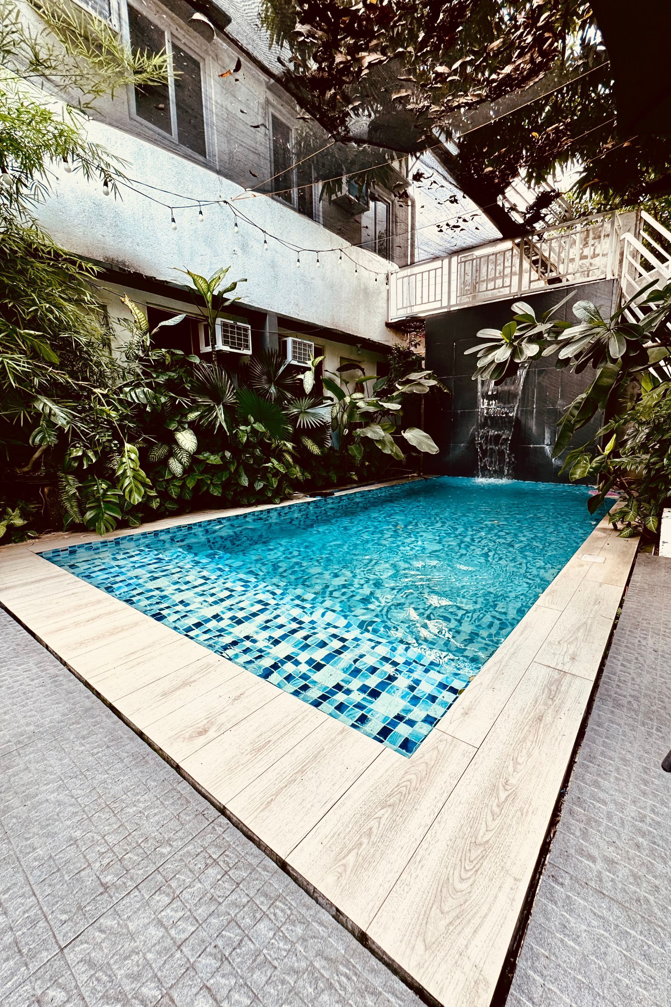 Piscina rectangular con borde de azulejos, rodeada de abundante vegetación y una terraza de madera.
