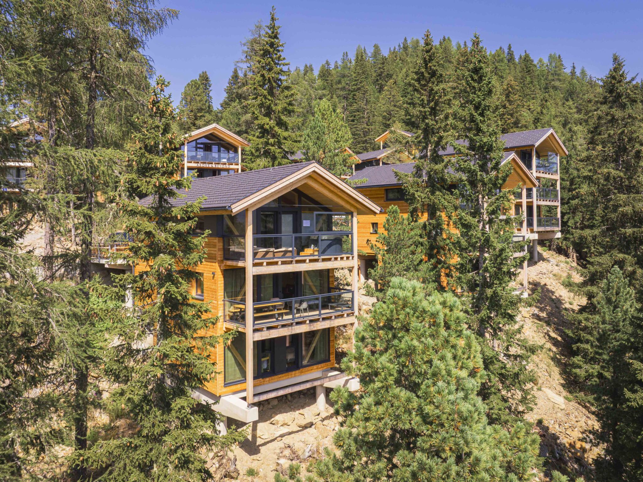 Un chalet à étages, doté d’une façade en bois, de grandes fenêtres et d’un balcon.