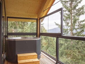 Eine Holzterrasse mit Whirlpool und Blick auf Wald und Berge.