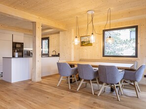 Ein modernes Interieur mit einer Holzes Essecke, einer Küche mit Edelstahlgeräten und einem großen Fenster mit Blick auf Bäume.
