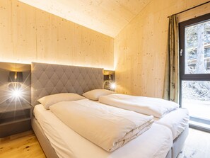 Une chambre à coucher comprenant un lit, une tête de lit, des lampes de chevet et une fenêtre donnant sur des arbres.