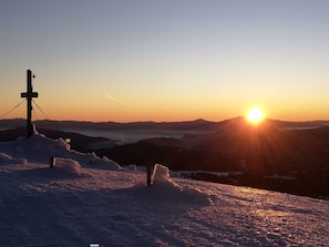 Schneebedeckte Landschaft mit Sonnenuntergang, Bergen im Hintergrund und einem Strommast mit Lampe.