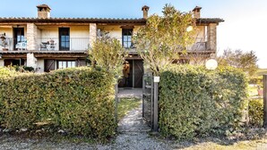 A two-story building with a balcony, a gate, and a pathway leading to the entrance. - GuestHost - Nestled between the Crete Senesi and Chianti, this home offers a breathtaking view of the countryside and Siena, just a 10-minute drive away. Part of a renovated historic farmhouse, it is a well-furnished townhouse with a private garden and v (Castelnuovo Bardenga)