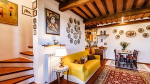 A living room with a yellow sofa, a dining table with chairs, a staircase, and a kitchen in the background. - GuestHost - Nestled between the Crete Senesi and Chianti, this home offers a breathtaking view of the countryside and Siena, just a 10-minute drive away. Part of a renovated historic farmhouse, it is a well-furnished townhouse with a private garden and v (Castelnuovo Bardenga)