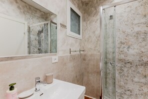 Une salle de bain avec un lavabo blanc, un miroir, une fenĂȘtre et une cabine de douche en verre.