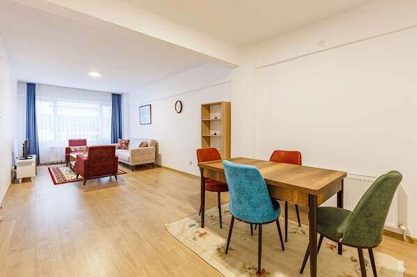 Una sala de estar moderna con una mesa de comedor de madera, sillas rojas y azules, un sofá y una estantería.